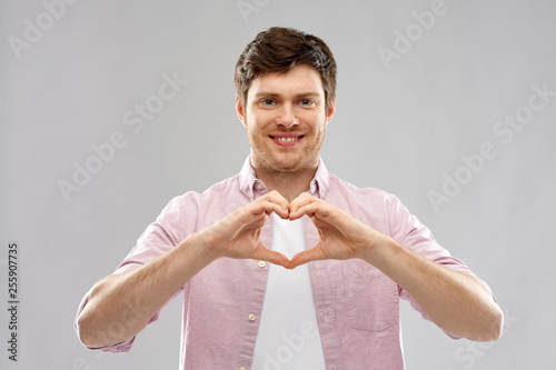 love, charity and valentine's day concept - smiling man making hand heart gesture over grey background