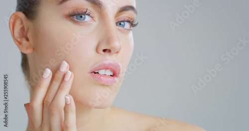 Portrait close up of woman with beautiful face and perfect skin just cleaned from impurities touching it gently with hand to show how soft and smooth it is.