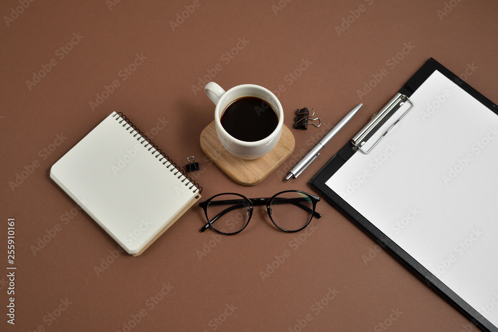 Flat lay, top view office table desk. Workspace with blank clip board, notebook, eyeglasses, office supplies, pen and coffee cup on brown background. Blog concept Flat lay, top view office table desk. Workspace with blank clip board, notebook, eyeglasses, office supplies, pen and coffee cup on brown background. Blog concept