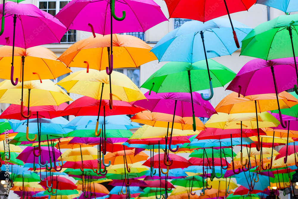 A place in the center of Paris with colorful umbrellas instead of ceiling. Yellow red pink blue green orange. Sunlight coming from the top. Wind is blowing