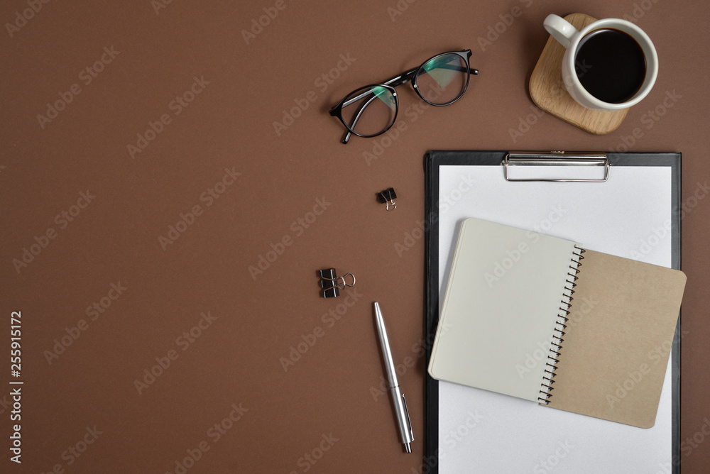 Mock up workspace with blank clip board, office supplies, pen, coffee cup, notepad and eyeglasses on brown background. Flat lay, top view, copy space Mock up workspace with blank clip board, office supplies, pen, coffee cup, notepad and eyeglasses on brown background. Flat lay, top view, copy space
