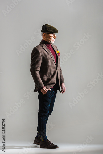 stylish middle aged man in glasses and cap standing with hand in pocket on grey © LIGHTFIELD STUDIOS