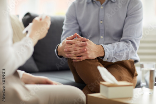 Crossed hands on knees of contemporary psychologist during discussion of patient problem on couch