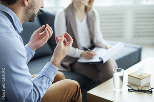 Fotografie Young man explaining his problems to counselor while sitting in front of her by