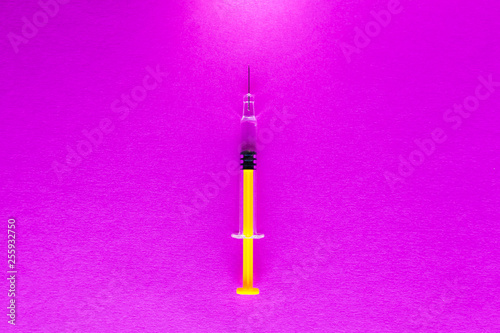 Yellow glass medical syringe over pink background © andrey_orlov