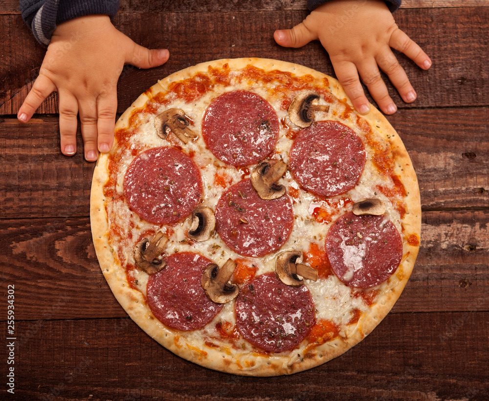 Children's hands ready to grab pepperoni pizza on rustic, vintage style wood background. Top view