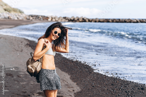 Pretty brunette long hair girl have fun on the beach with black sand near sea.