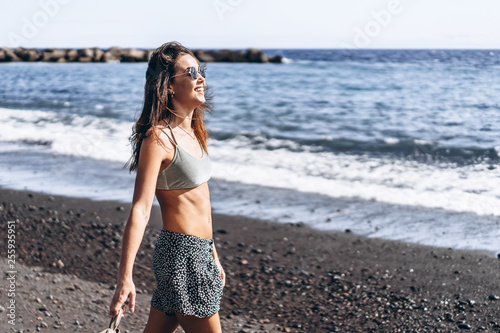 Pretty brunette long hair girl have fun on the beach with black sand near sea.