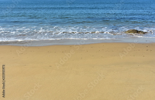 Beach with golden sand and blue sea with foam.