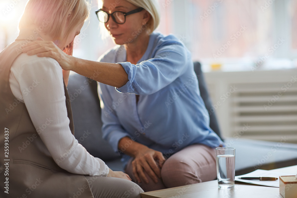 Obraz premium Mature psychologist supporting young patient while sitting next to her and keeping hand on female shoulder