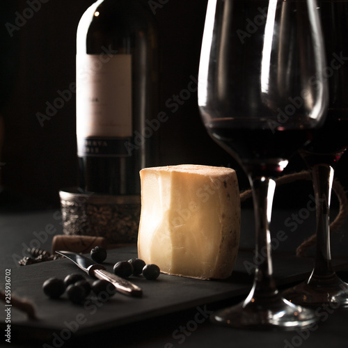 cheese board with hard mature cheese, antique knife and blueberries, glasses of wine, a bottle of wine. Selective focus. photo