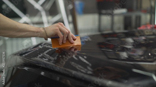 professional applying protective film to the red car. Master glues a protective film on the hood of the car