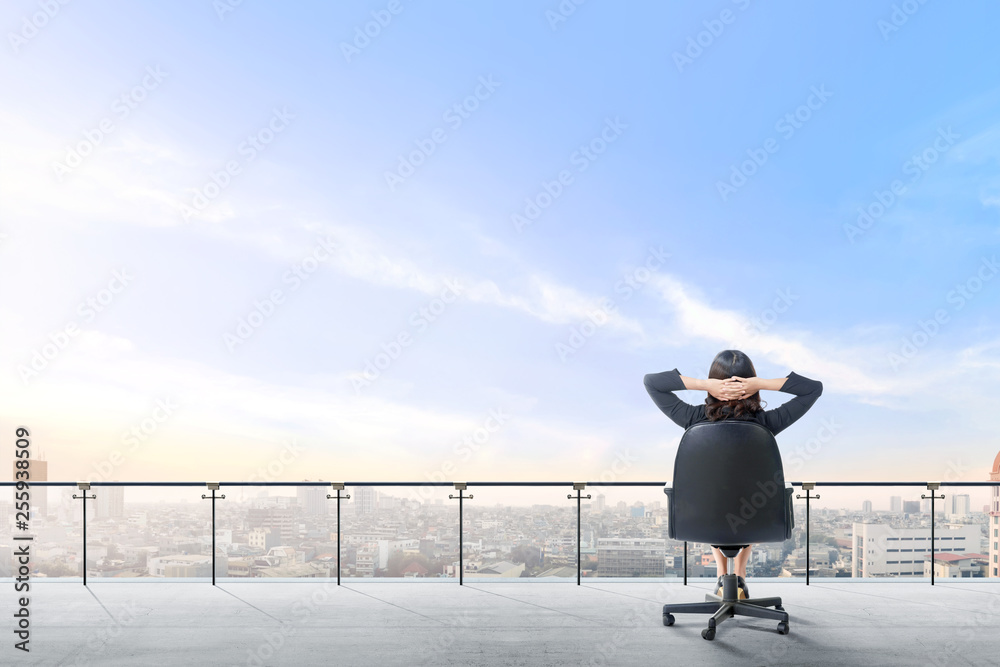 Rear view of asian business woman sitting on the office chair in modern terrace relax and looking at view on the city