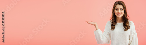 panoramic shot of beautiful woman in white sweater pointing with hand isolated on pink