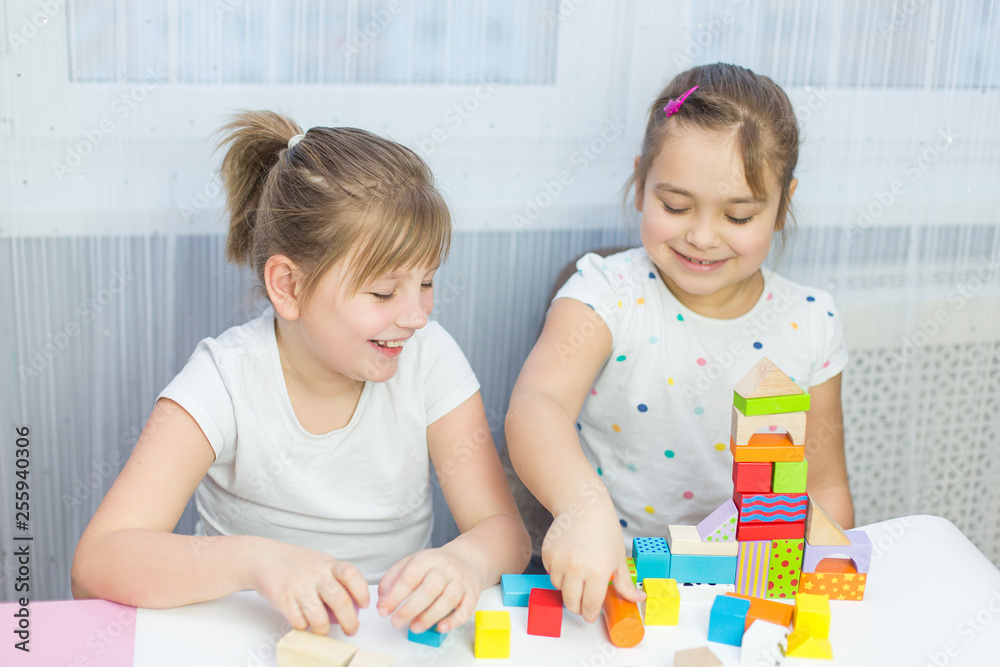 Fototapeta premium Children play with an educational toy on table in the children's room. Two kids playing with colorful blocks. Kindergarten educational games
