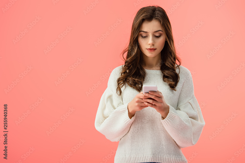 beautiful young woman in white sweater holding smartphone isolated on pink