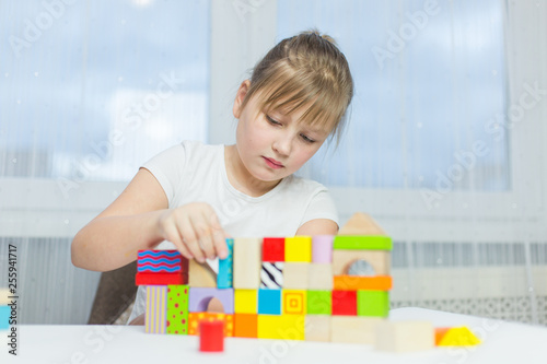 Schoolgirl girl play with educational toy on table in the children's room. Two kids playing with colorful blocks. Kindergarten educational games