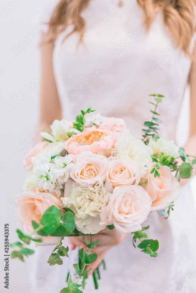 The bride is holding a gorgeous wedding bouquet in pastel colors of peonies and roses