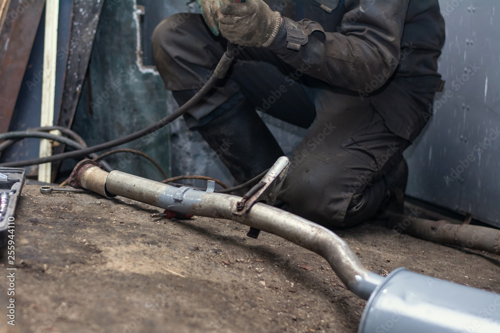 repairing of corrugation muffler of exhaust system in car workshop - serviceman welds the old silencer on car by argon welding