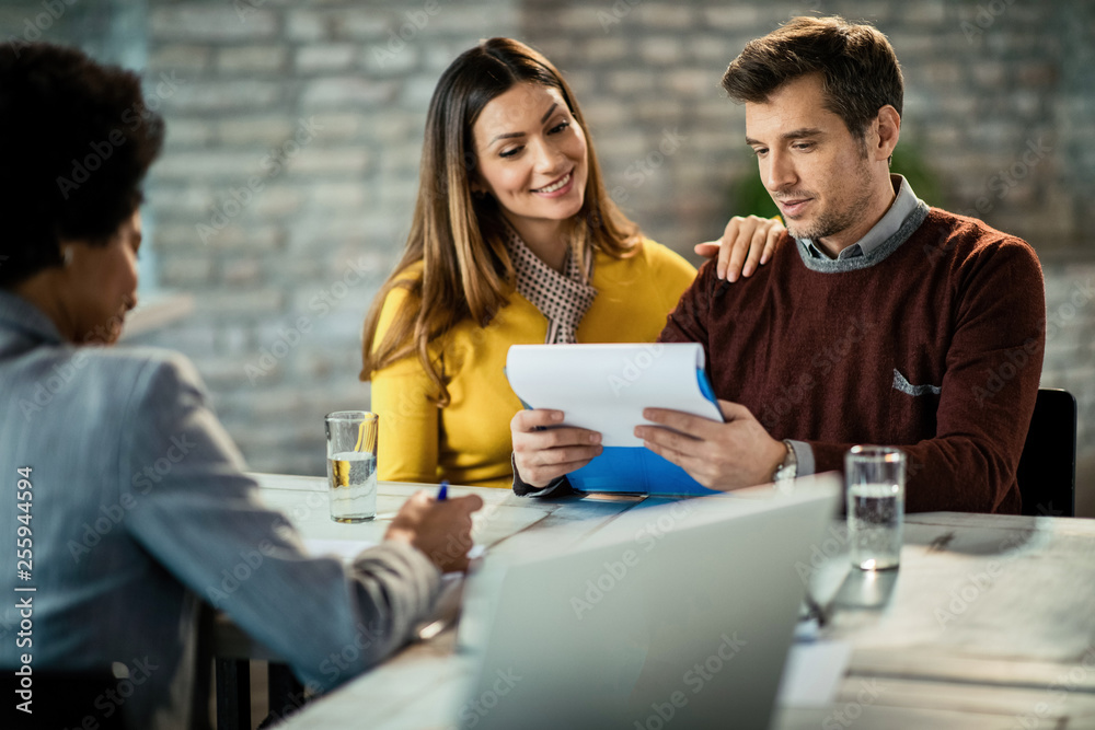 Fototapeta premium Happy couple reading reports while having a meeting with financial advisor in the office.