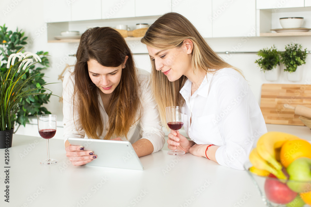 two beautiful european women drinking wine and shopping online using tablet