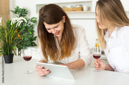 two beautiful european women drinking wine and shopping online using tablet