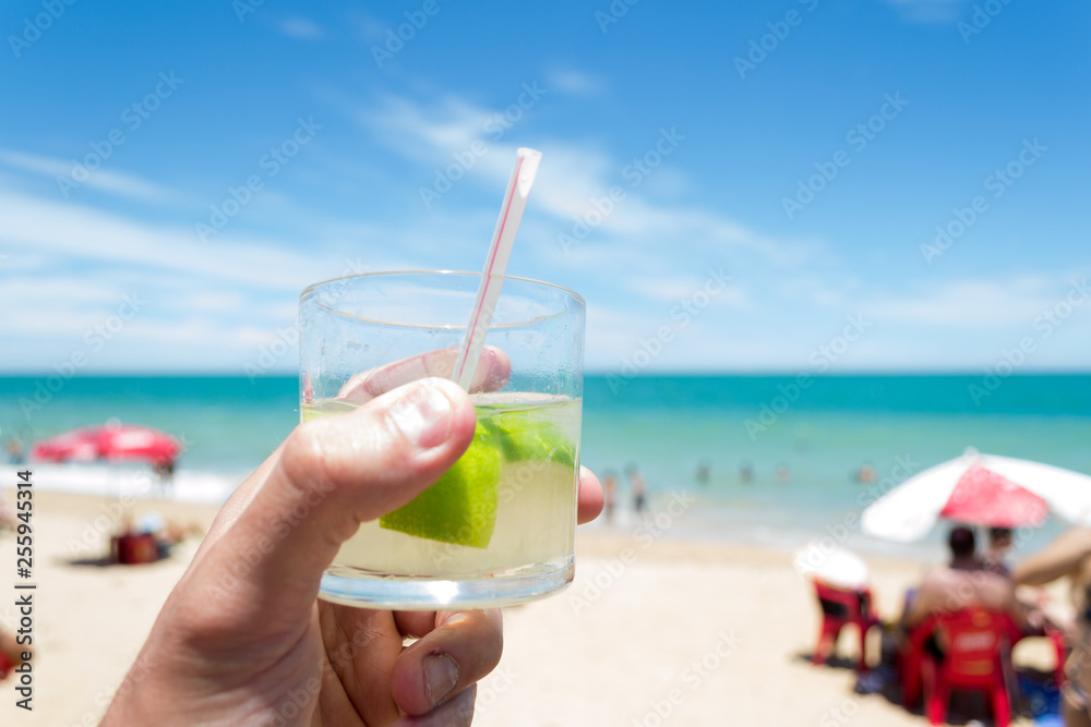 Obraz premium Relax time at the beach in Marataizes, a little seaside village in the Espirito Santo state in Brazil. A hand holding a caipirinha a typical local drink