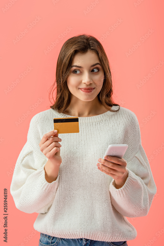 cheerful brunette girl holding credit card and smartphone isolated on pink cheerful brunette girl holding credit card and smartphone isolated on pink