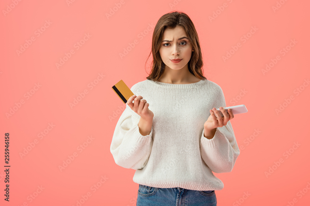 confused brunette girl holding credit card and smartphone isolated on pink confused brunette girl holding credit card and smartphone isolated on pink