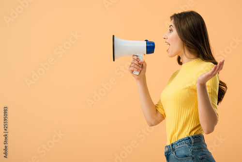 Side view of pretty brunette woman screaming in loudspeaker isolated on orange
