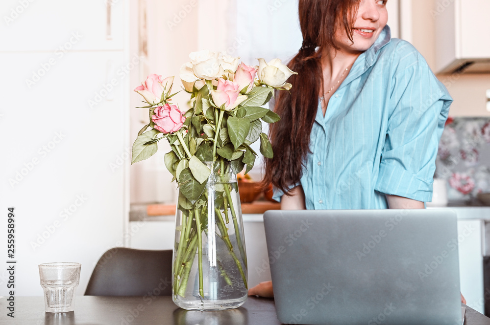 Young beautiful woman working at home at the computer. Home office for remote work. Business lady in a comfortable house and flowers on the table. Free space for text. Light effect on the photo.