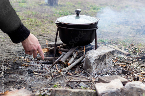 soup cooked in katla on a fire. A person puts firewood in the fire