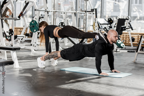 Athletic couple doing difficult sport exercise where the girl stands in the plank on a man who stands in the plank in the modern gym
