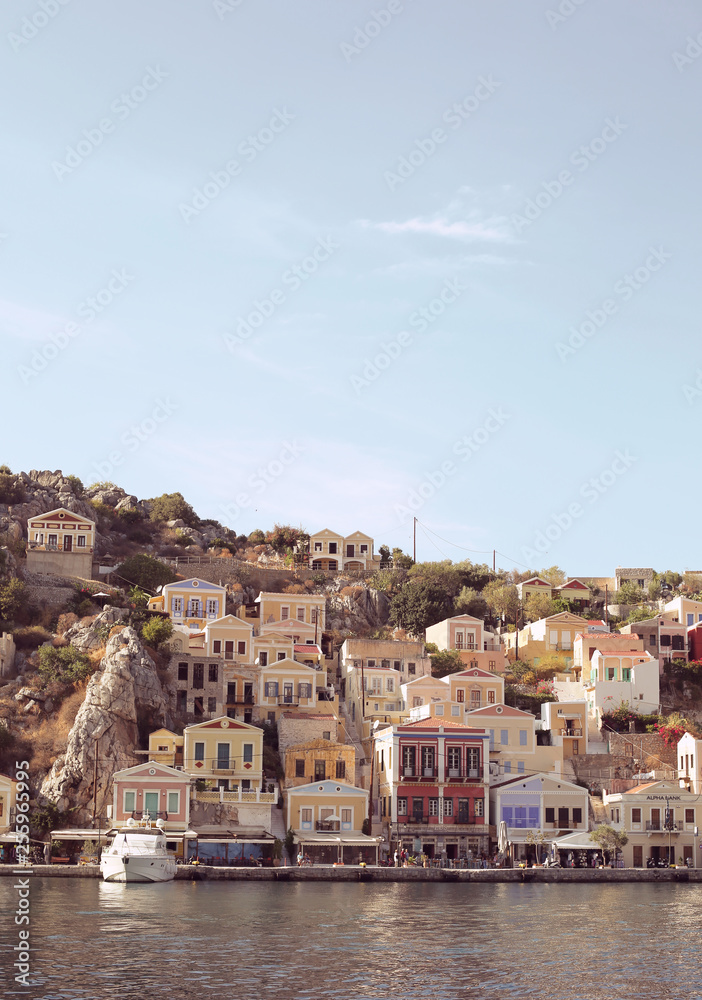 Colourful houses of the picturesque Symi island, holiday island of Dodecanese group close to Turkish coast north of Rhodes. Sunny summer evening. Dusk light. Greece. Landscape view from the water.   