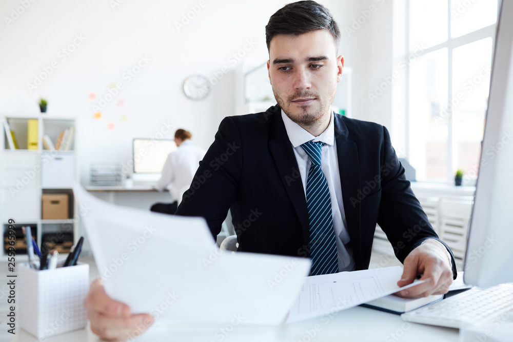 Serious young banker or broker reading papers and preparing all necessary documents for making deal with client Serious young banker or broker reading papers and preparing all necessary documents for making deal with client