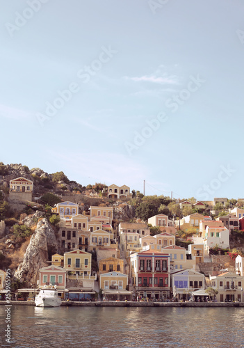 Colourful houses of the picturesque Symi island, holiday island of Dodecanese group close to Turkish coast north of Rhodes. Sunny summer evening. Dusk light. Greece. Landscape view from the water. 