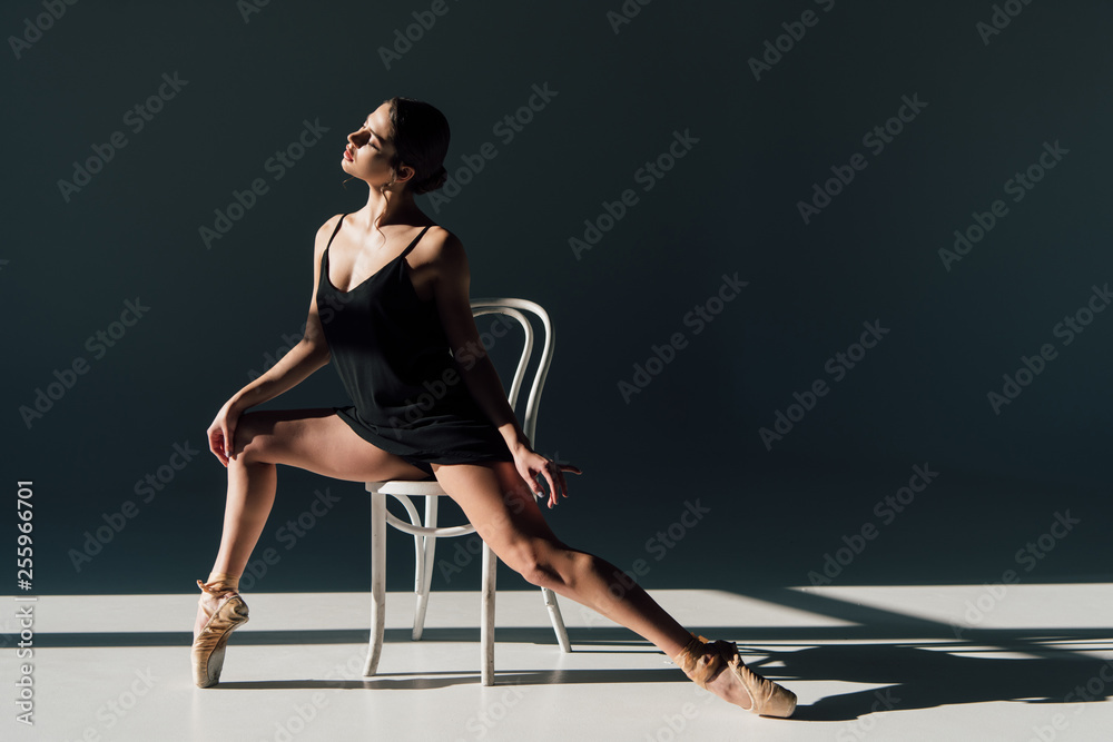 beautiful ballerina in black dress stretching on white chair