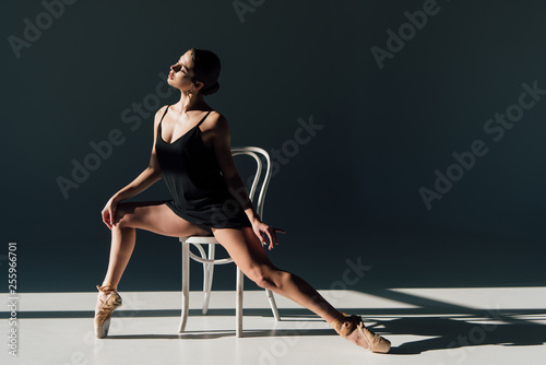 beautiful ballerina in black dress stretching on white chair