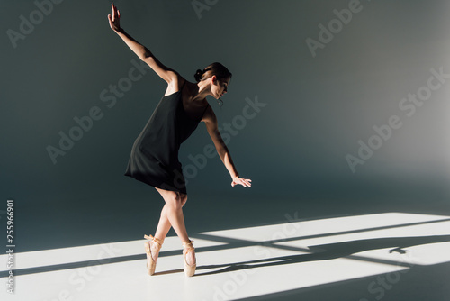 graceful young ballerina in black dress dancing in sunlight