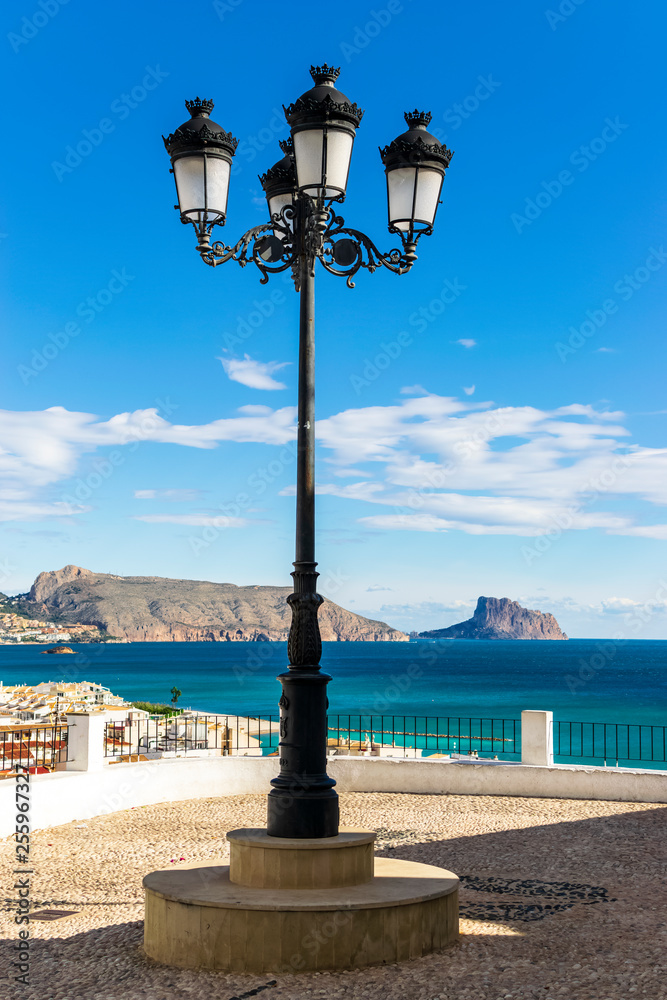 Vertical photograph of the Alto of a small coastal town with a protagonist lamppost looking towards the sea. Photograph taken in Altea, Alicante, Spain.