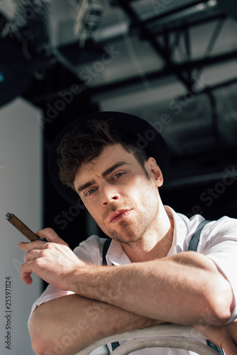 handsome pensive man smoking cigar and looking at camera