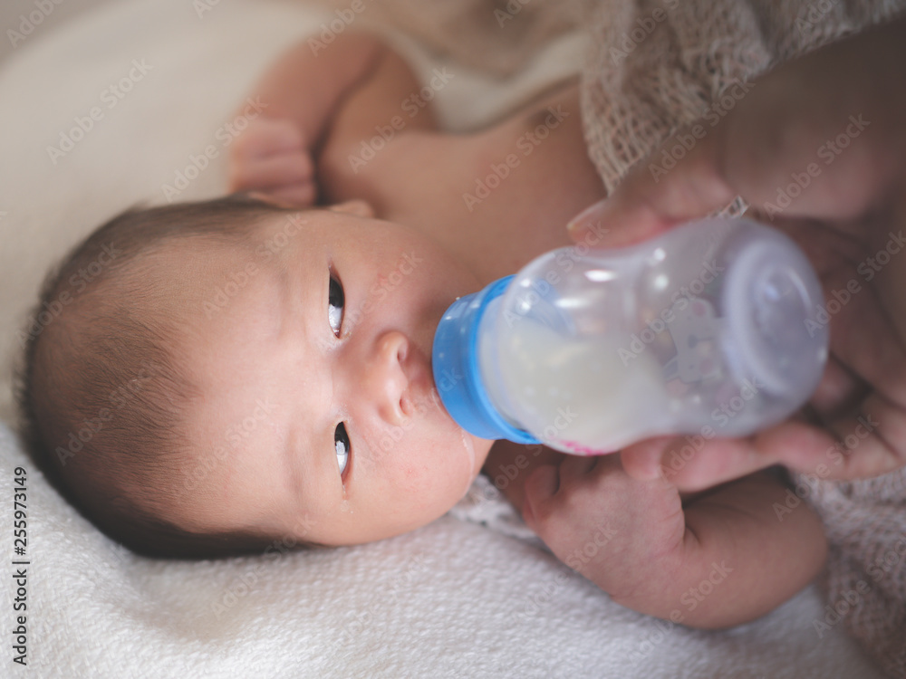 Close up of Asian female newborn baby lying in bed and Suck milk Bottle in home with sunlight in the morning. Cute little girl three weeks old. Baby health concept Close up of Asian female newborn baby lying in bed and Suck milk Bottle in home with sunlight in the morning. Cute little girl three weeks old. Baby health concept