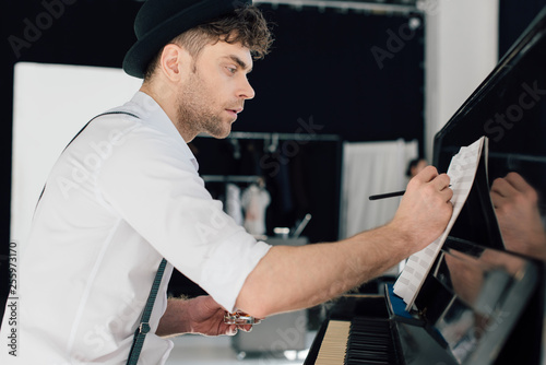 selective focus of handsome composer writing in music book while sitting at piano at home