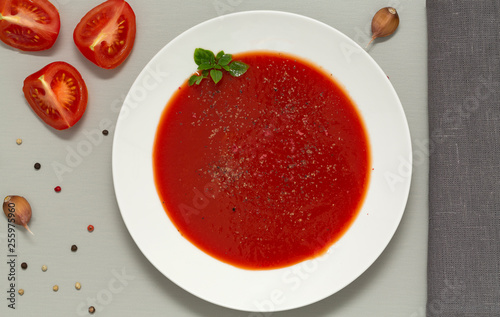 Tomato soup in a white bowl on grey background. Delicious soup of tomatoes and fresh herbs with garlic and spices. Top view.