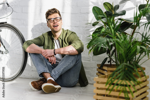 Photography handsome man in green shirt, jeans and glasses smiling and sitting on floor near