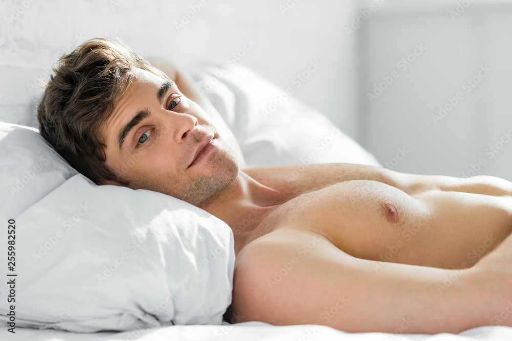 handsome man lying on bed and pillow with bare torso in bedroom handsome man lying on bed and pillow with bare torso in bedroom