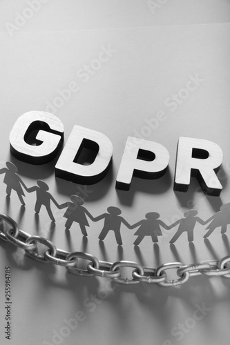 Wooden GDPR letters in front of human paper figures and metal chain. General data protection concept.