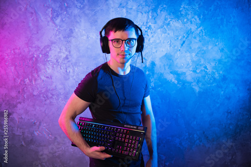 Professional Boy Gamer holding gaming keyboard over colorful pink and blue neon lit wall. Gaming gamers concept photo