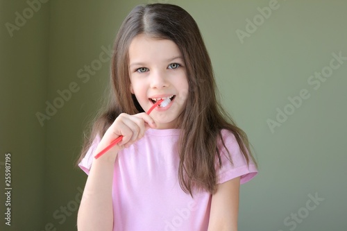 Girl brushing her teeth. Long haired smiling beautiful caucasian white girl brushing teeth with pink toothbrush on green background. Green eyed cute child in pink tshirt doing her morning hygiene. 