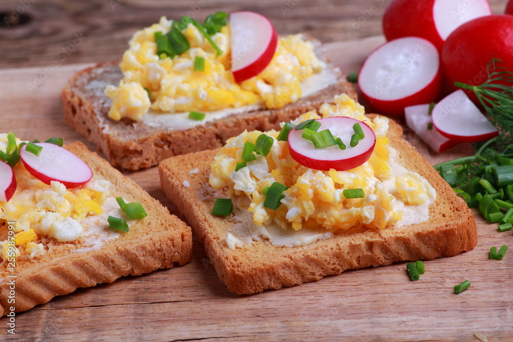 Scrambled eggs with fresh radish and chives on toasted bread for breakfast